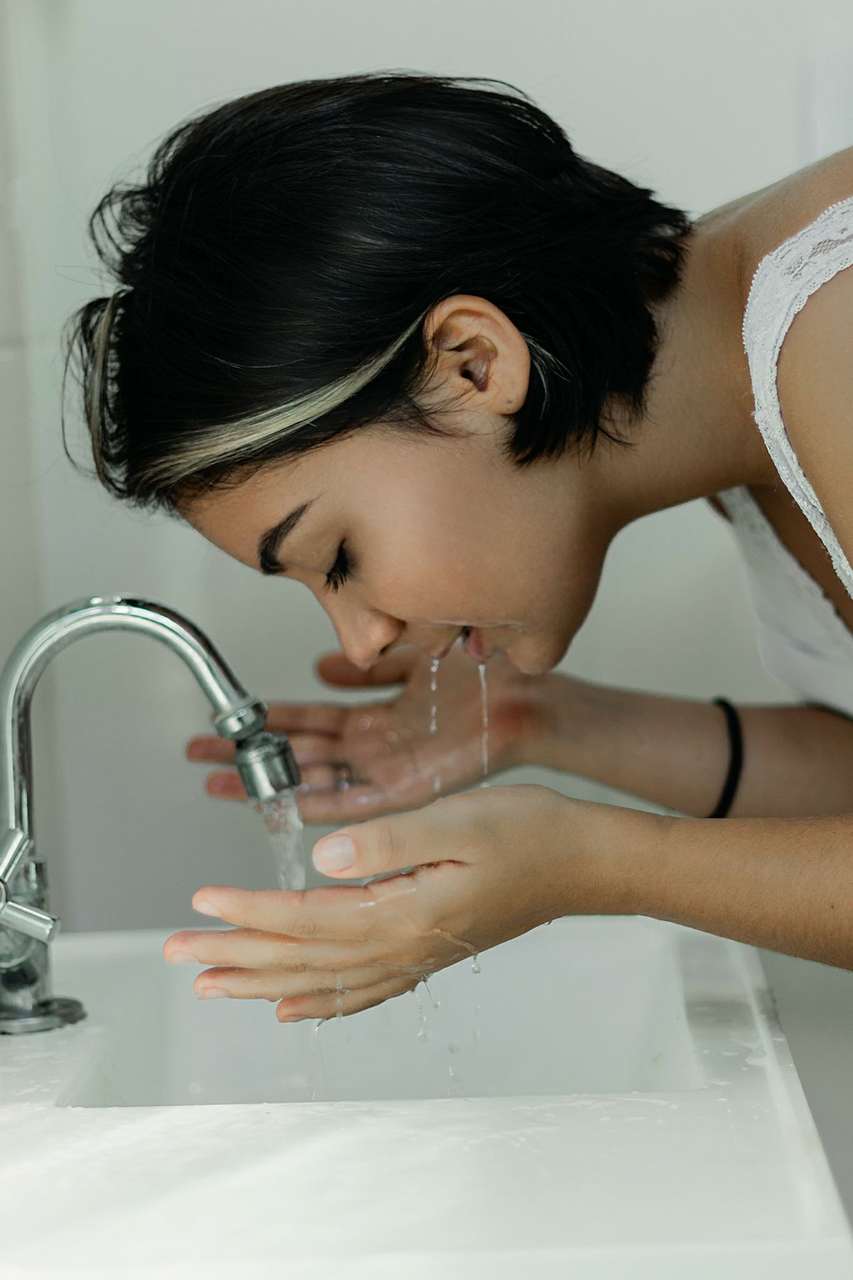 A woman with short hair gently washes her face at a bathroom sink, embracing a clean and refreshing start to the day.