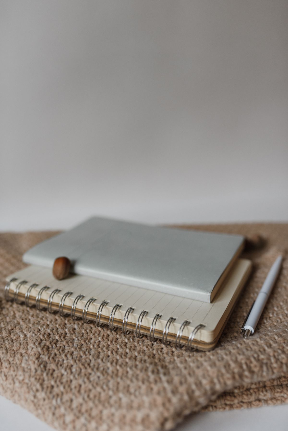 A minimalist composition featuring notebooks and a pen on a woven surface, perfect for office or study themes.